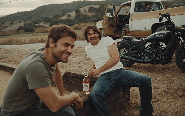 Wesley and Somerhalder sit by a motorcycle with a bottle of Brother's Bond Bourbon