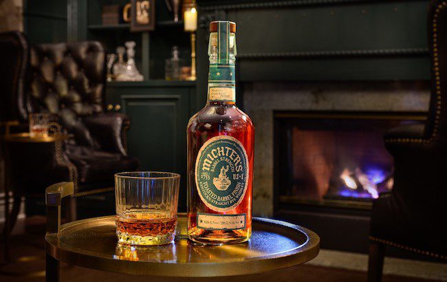 Bottle of rye whiskey in front of a fireplace and leather arm chairs