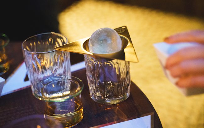 An ice sphere hovers above a glass of whisky