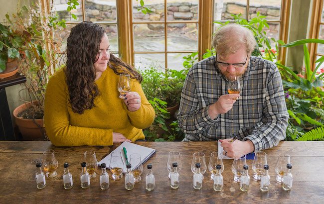 A man and woman sit at a table smelling whisky samples