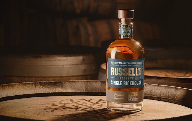 A bottle of bourbon sitting on a whiskey barrel 