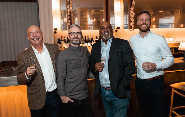 Four men holding drinks at a bar