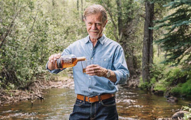 A man pours a whiskey while standing in the middle of a river