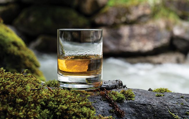 Glass of scotch single malt whisky with fast flowing mountain river on background, Scotland