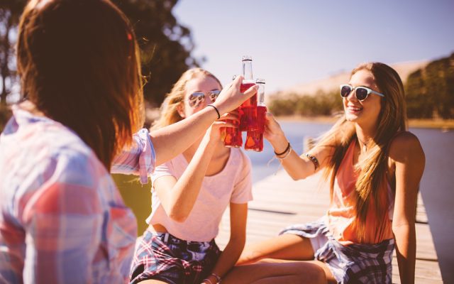 Teenaged girls saying cheers together with pink alcopops outdoors relaxing on a summer vacation