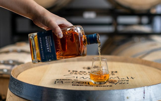 Bottle of whiskey being poured into a glass on top of a barrel