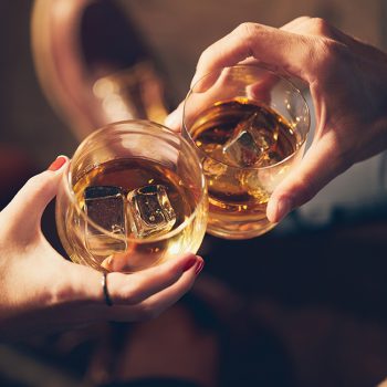 A couple makes a toast with two glasses of whiskey