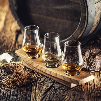 Glencairn tasting whiskey cups with wooden barrel, peat and barley next to them.