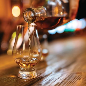 Pouring Irish whiskey in glass on bar counter.