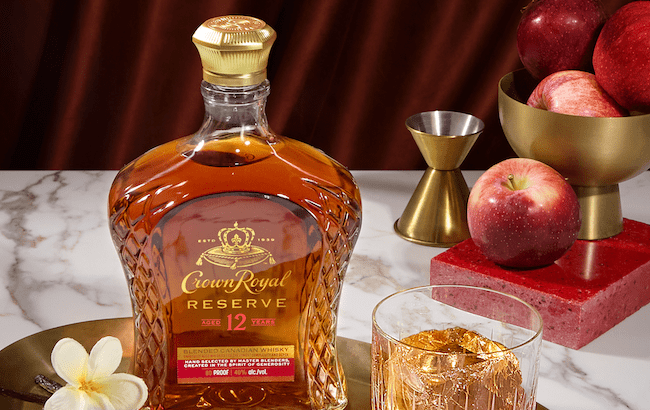 A bottle of Crown Royal Reserve 12 year old alongside apples, vanilla, and a glass of whisky