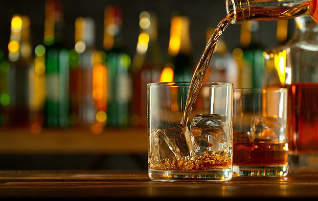 Close-up of pouring whiskey or rum on the bar, dark toned background