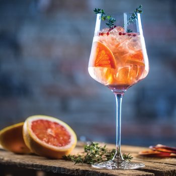 Cocktail drink on a old wooden board. Alcoholic beverage with tropical fruits red pepper herb and ice.