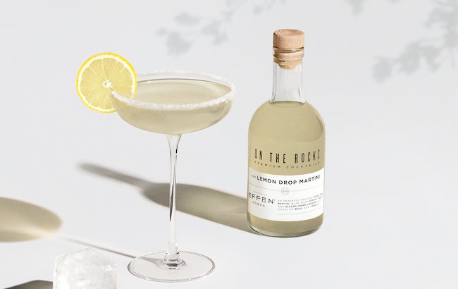 A garnished Lemon Drop martini in a glass beside a bottled cocktail of the same drink