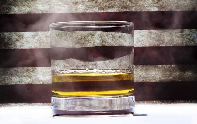A glass of whiskey in front of the stripes of an American flag