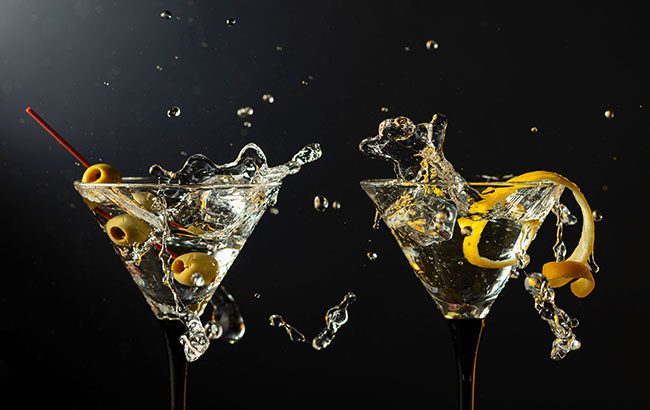 Classic dry martini cocktails with green olives and lemon peel on a black background. Martini with splashes. Free space for your text.
