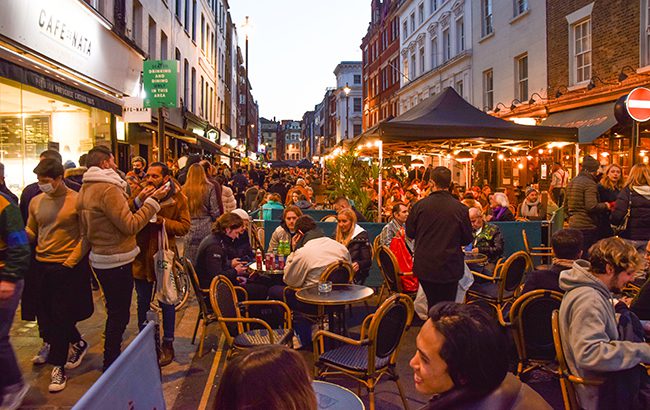 London, United Kingdom - April 16 2021: Busy outdoor street seating at bars and restaurants in Old Compton Street in Soho at night.