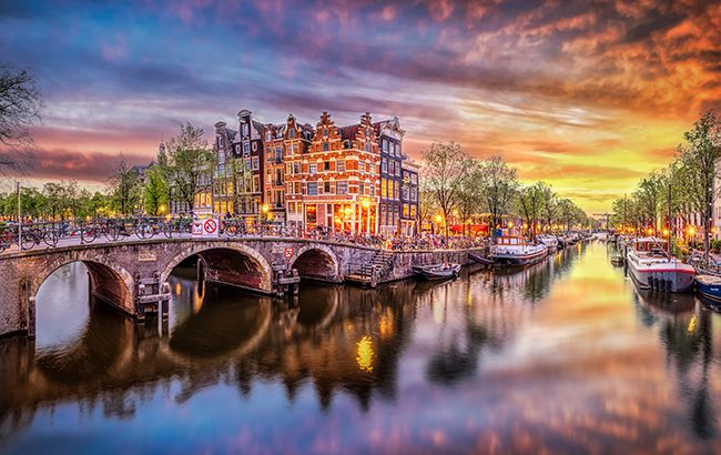 Sunset in Amsterdam. Panoramic view of the historic city center of Amsterdam. Traditional houses and bridges of Amsterdam town. A romantic evening and a bright reflection of houses in the water. European travel to the historic city. Europe, Netherlands, Holland