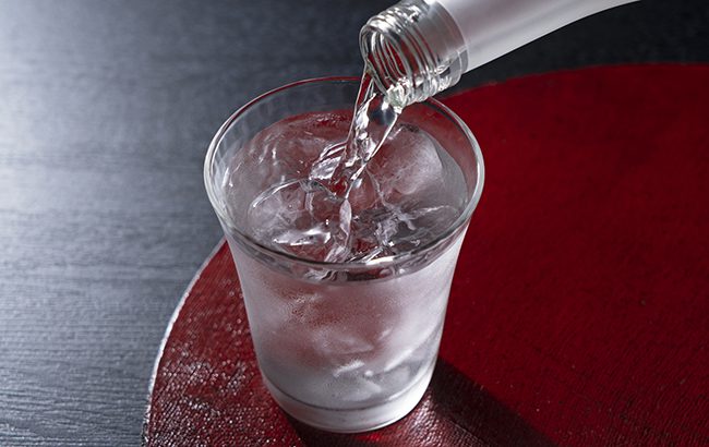 Shochu on a red tray against a black background. The moment of pouring in a bottle.