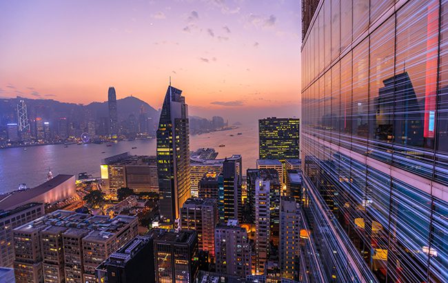 Spectacular aerial view of Victoria Harbor, skyscrapers and Hong Kong skyline at night. Skyline reflected in glass facade of a modern building. Asia